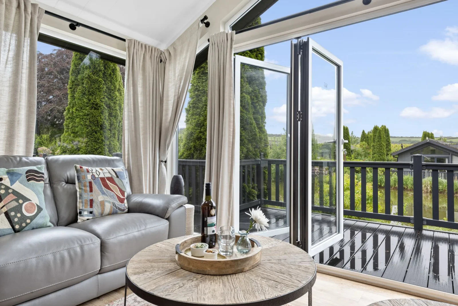 Sofa within lounge, bifold doors leading to decking area and coffee table - Brayford Lodge, Kentisbury Grange