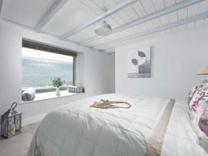 Large window with ocean view from bedroom, side table, lamps, towels  - Mermaids