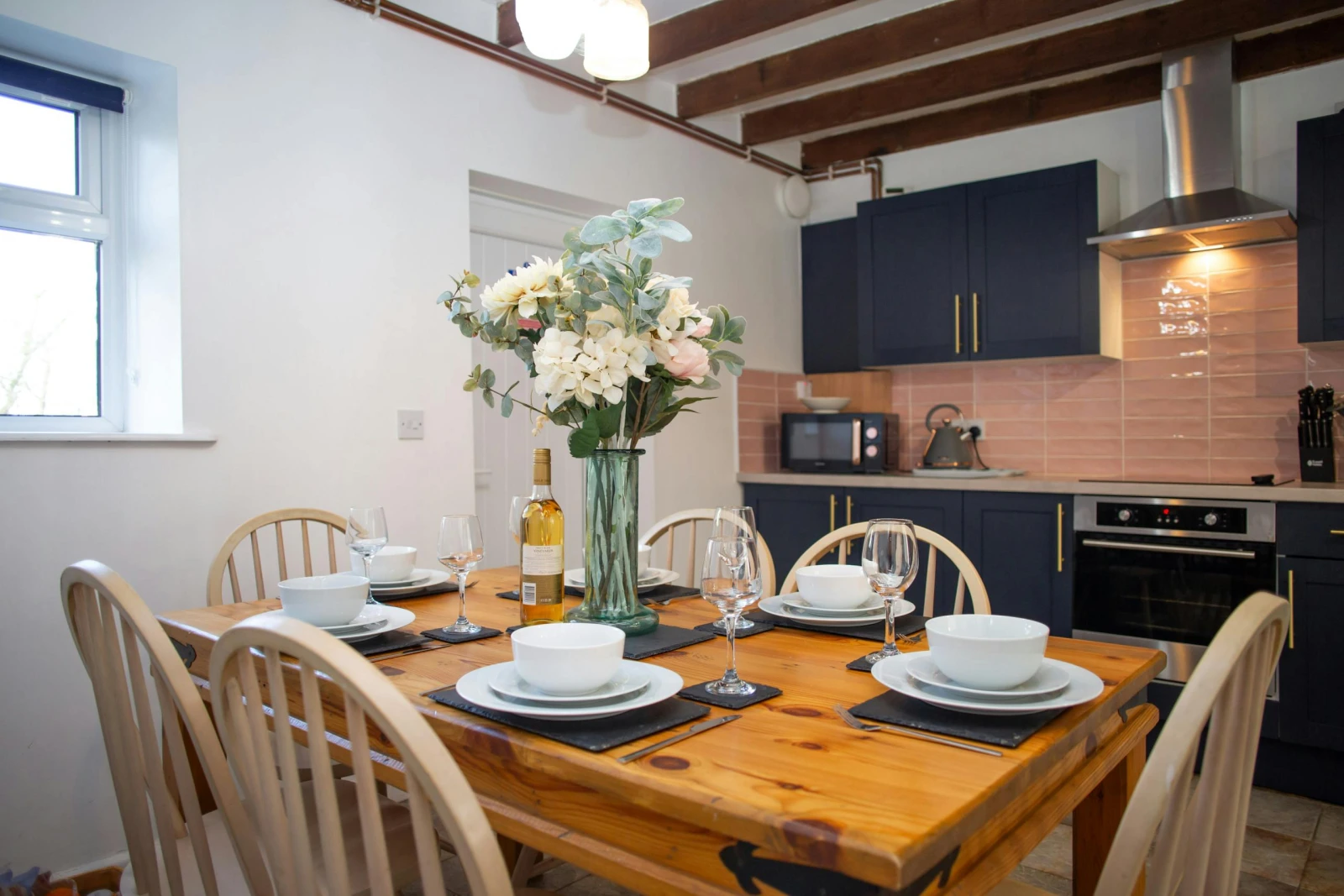Kitchen/diner with microwave, kettle, oven and dining table with six chairs laid for dinner