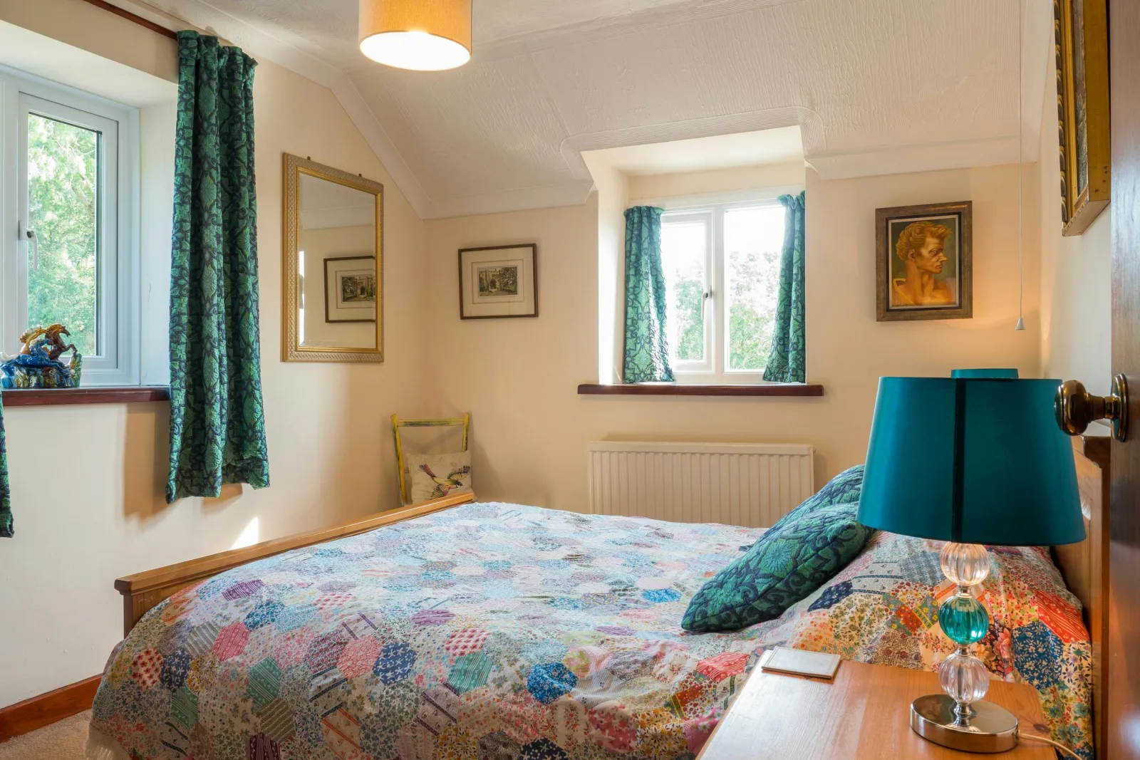 Double bed, bedside cabinet with lamp, small chair and mirror on wall