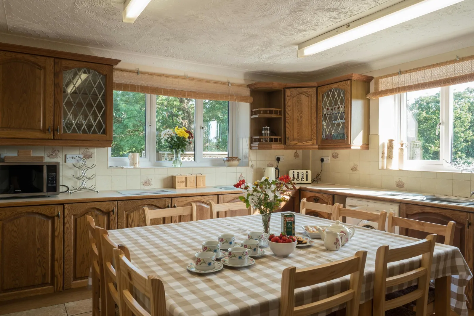 Kitchen cupboards, microwave, toaster, kettle, washing machine, sink, dining table with 10 chairs and two large windows