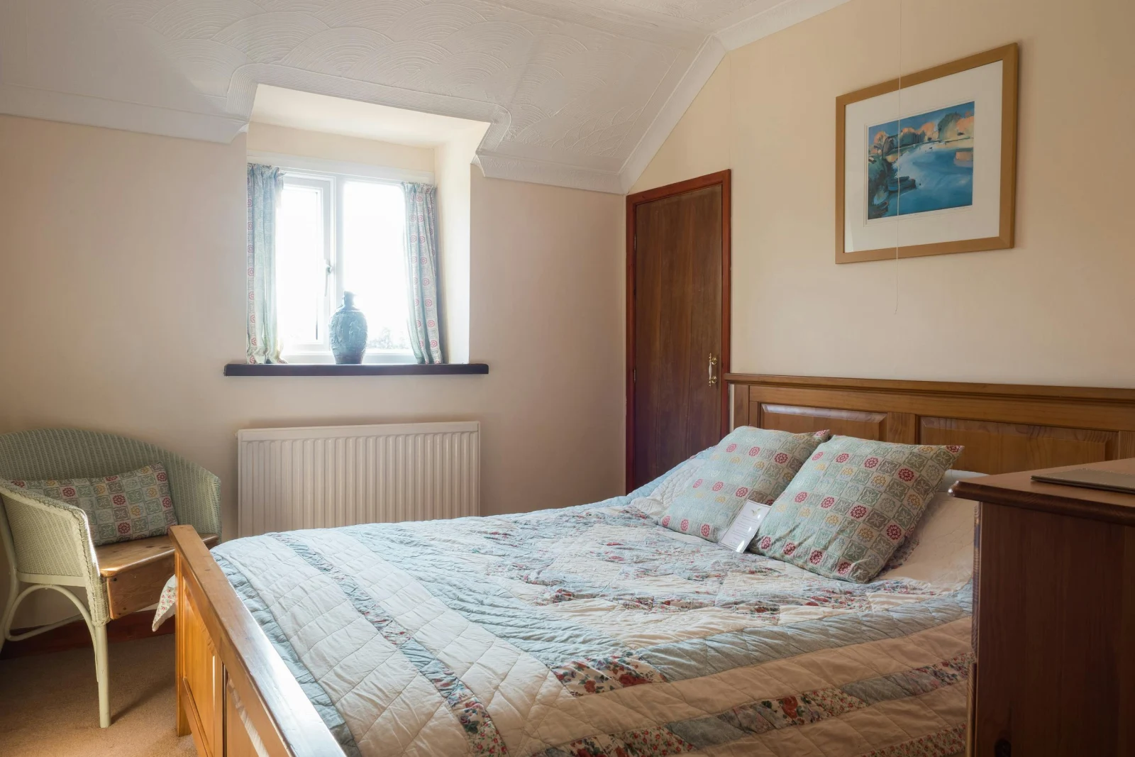 Double bed with quilted cover with a Lloyd Loom chair and chest of drawers