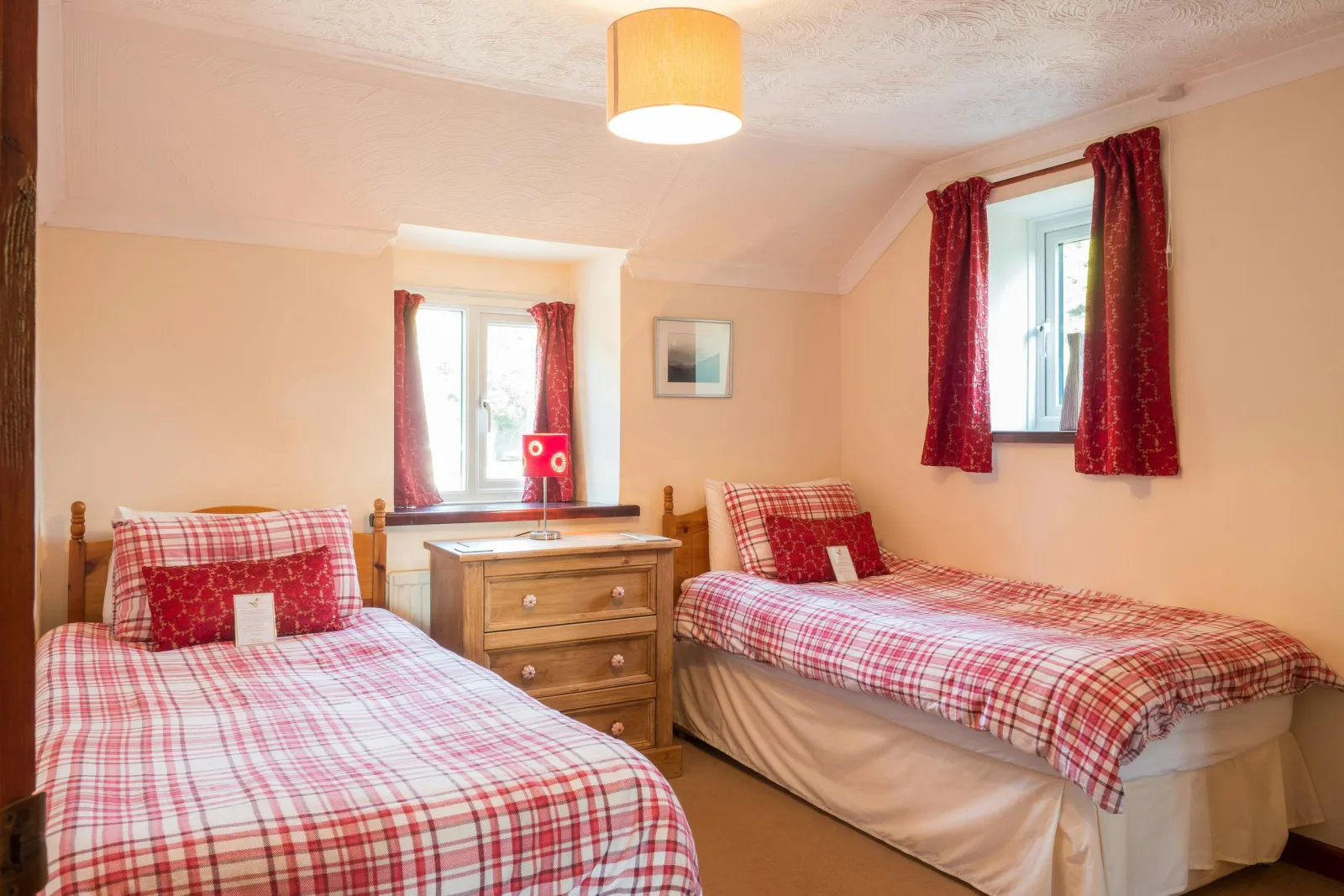 Twin single beds, chest of drawers with lamp and two windows