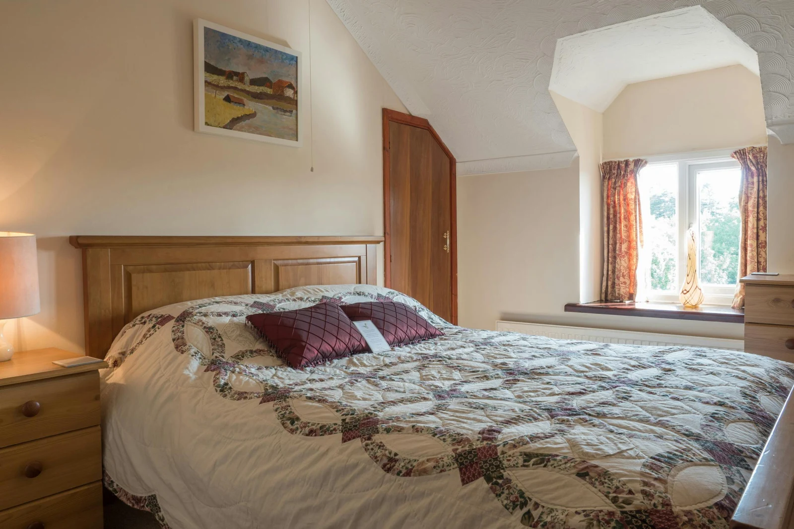 Double bed, bedside chest of drawers with lamp, larger chest of drawers and window