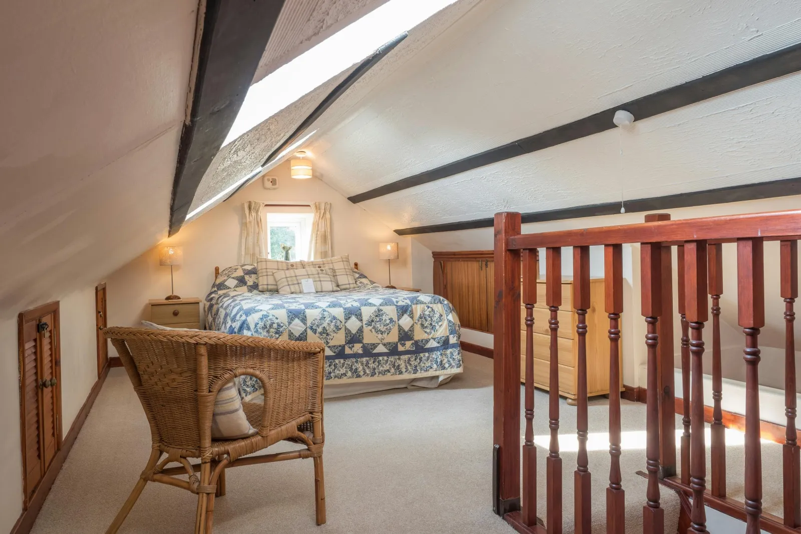 Attic double bed, cabinets with lamps, wicker chair and wooden bannister