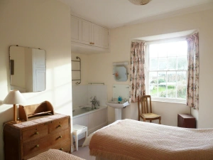 Twin single beds, chest of drawers with a lamp and mirror above, chair, bath and wash hand basin