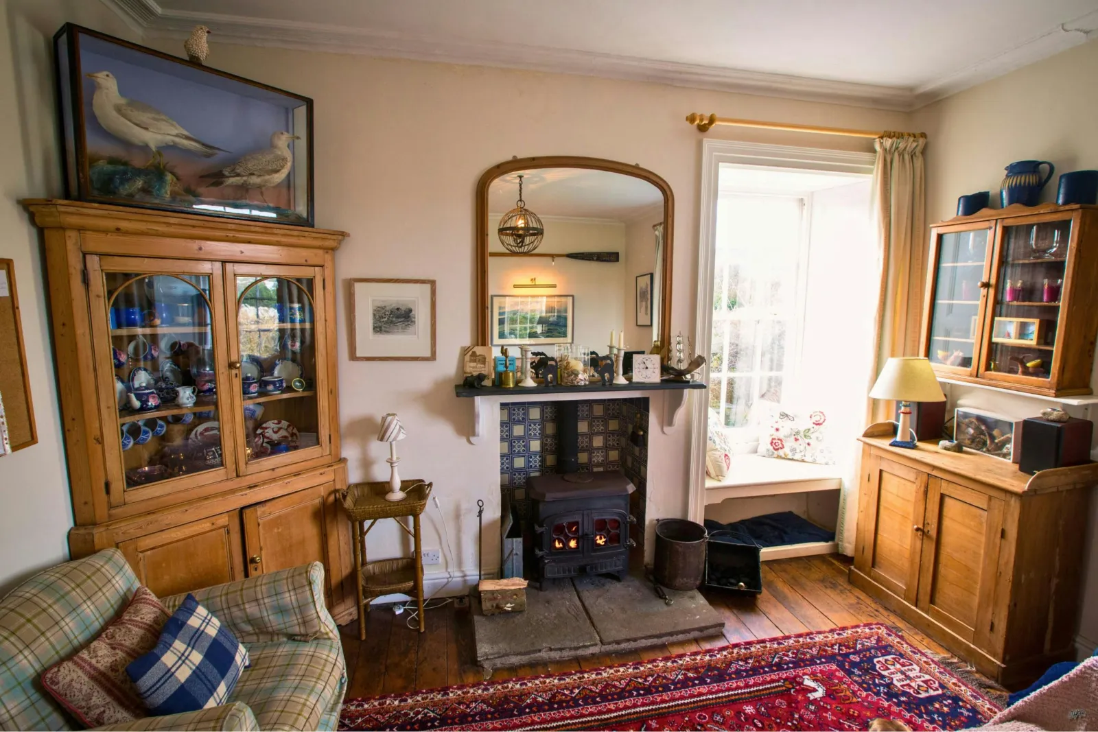 Drawing room: sofa, two wooden dressers, fireplace with log burner, large mirror and window