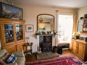 Drawing room: sofa, two wooden dressers, fireplace with log burner, large mirror and window