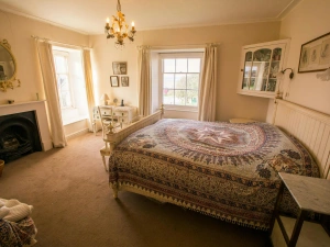Bedroom with open fireplace, bed with bedside tables, dressing table with a lamp and chair, two windows