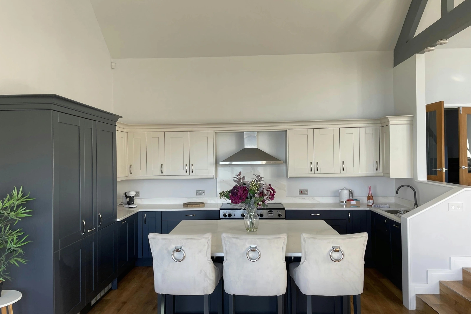 Open plan kitchen with breakfast bar island with three bar stools and fresh flowers in vase