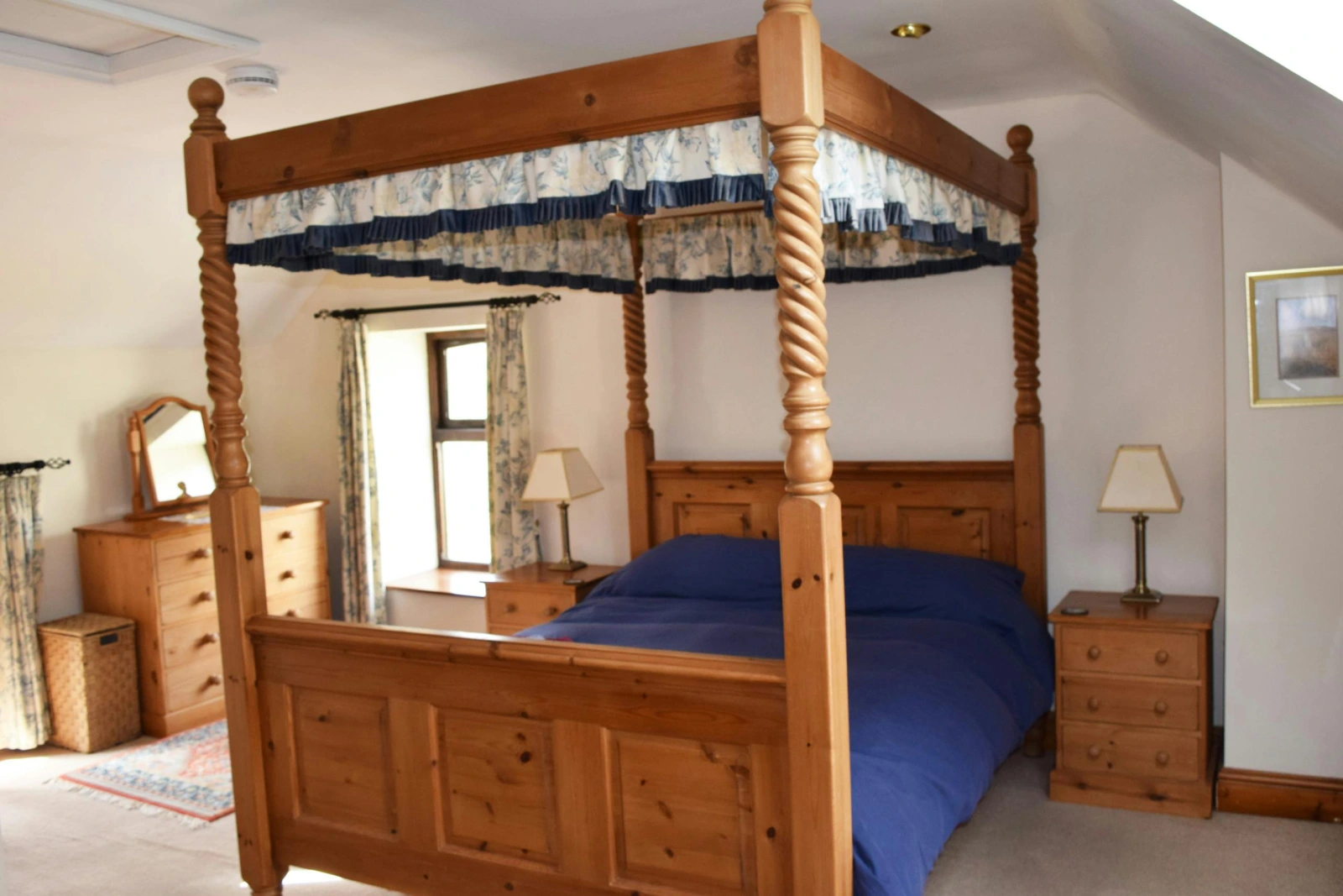 Bedroom with four poster bed, bedside drawers with lamps and chest of drawers with mirror
