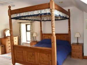 Bedroom with four poster bed, bedside drawers with lamps and chest of drawers with mirror