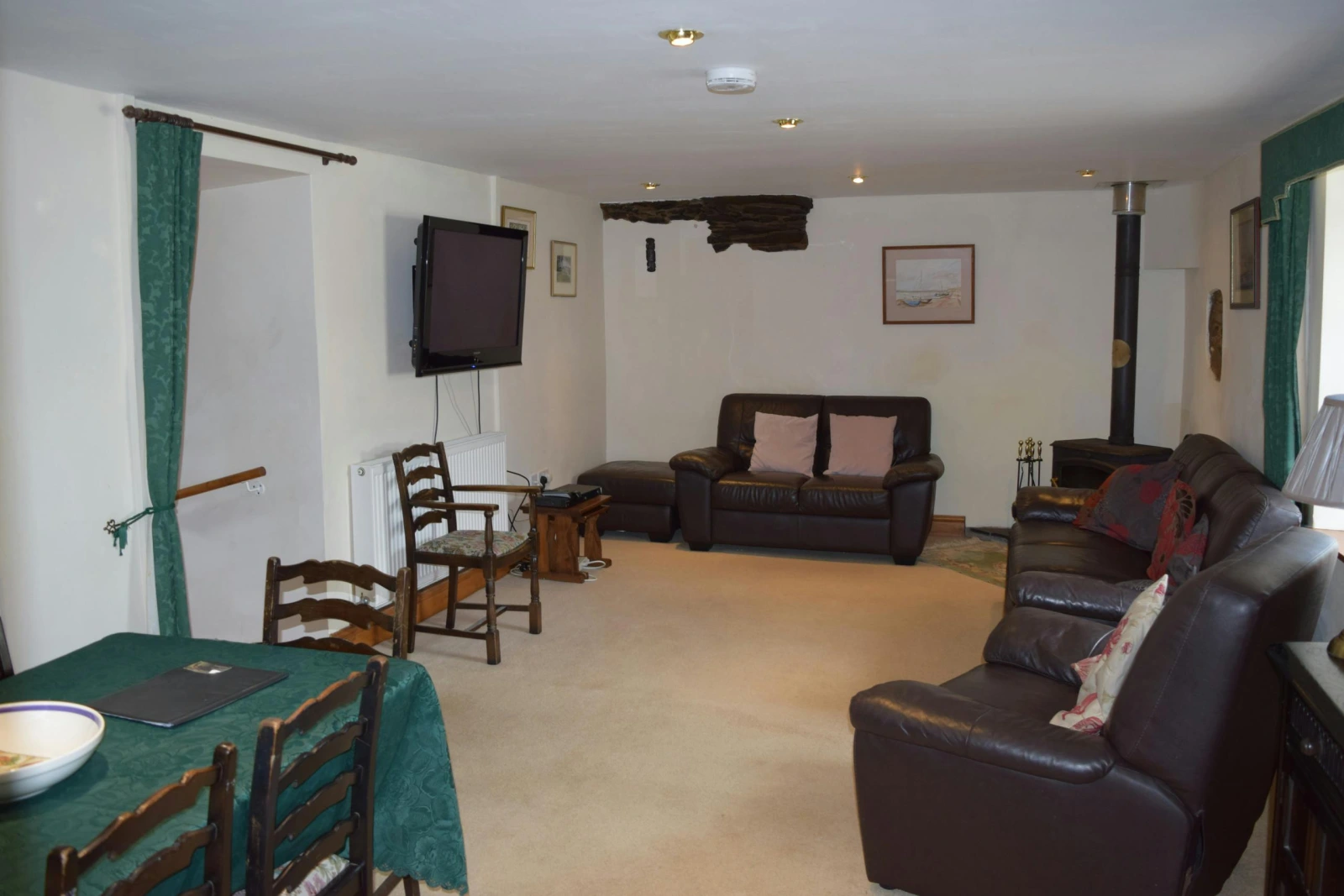 Sitting and dining room with log burner, sofas, armchair, dining table with chairs and wall mounted TV
