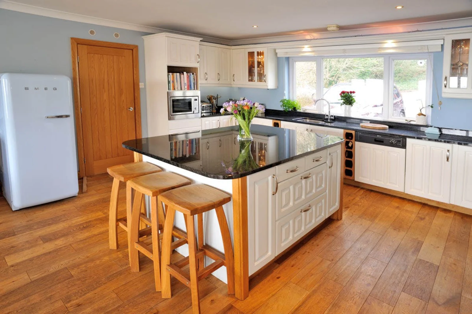 Island with bar stools in the centre of kitchen, Smeg fridge, dishwasher, toaster and built-in microwave