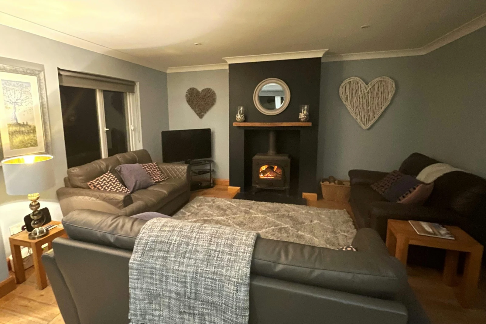 Three leather sofas with cushions, log fire, side tables with lamp, flat screen TV on shelving unit