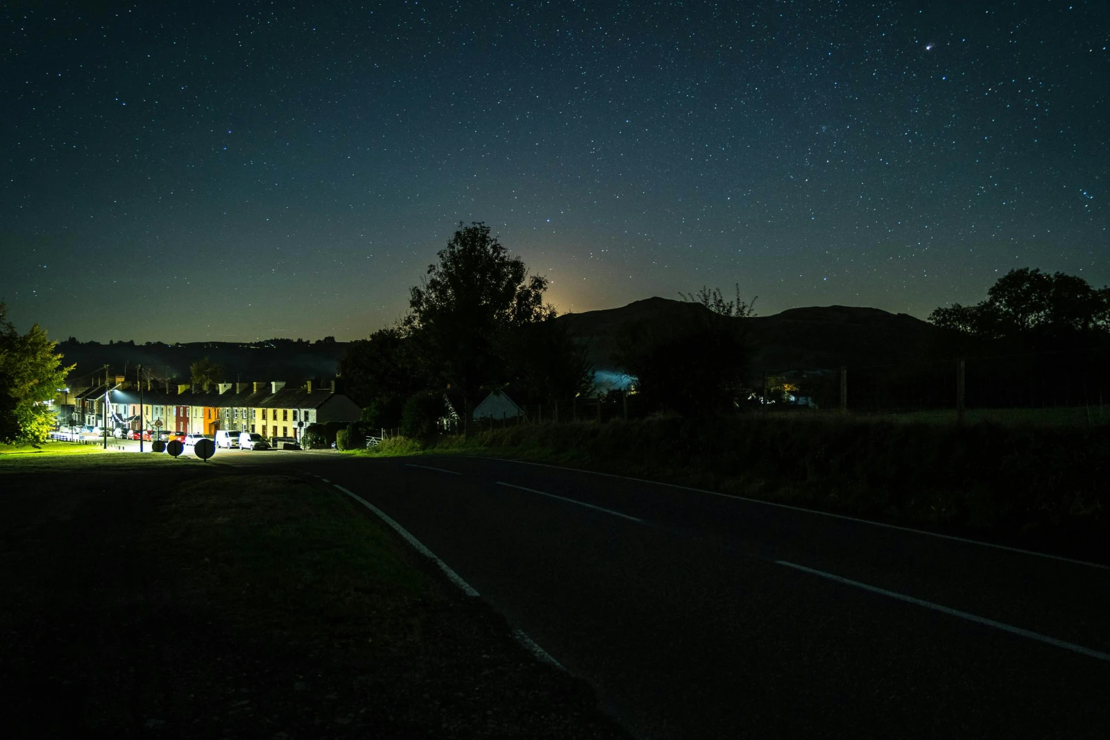 Night sky filled with stars and view of houses down the road lit up with street lights