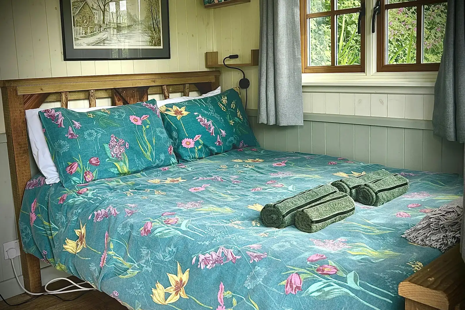 Double bed with teal floral bedding and folded towels by a window