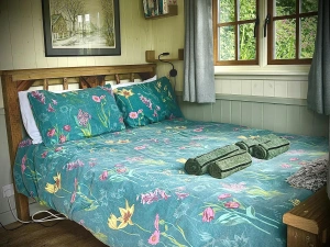 Double bed with teal floral bedding and folded towels by a window