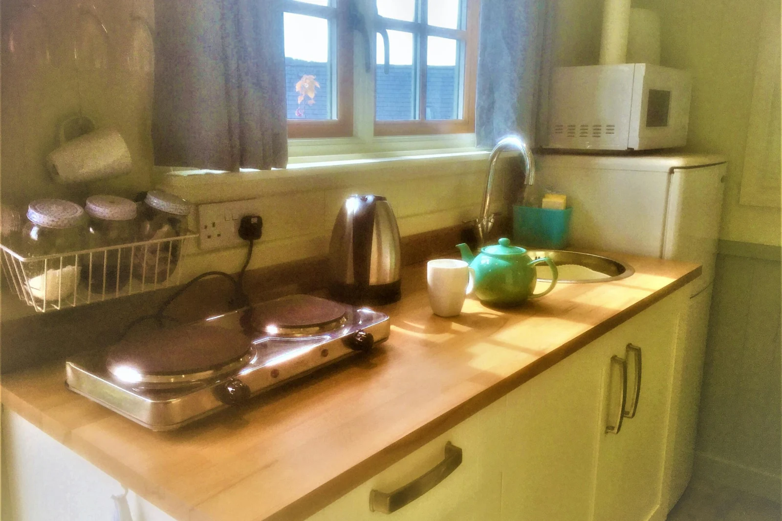 Kitchen with small hob, sink, kettle, fridge/freezer, microwave, various utensils and windows
