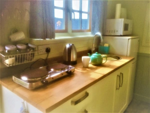 Kitchen with small hob, sink, kettle, fridge/freezer, microwave, various utensils and windows