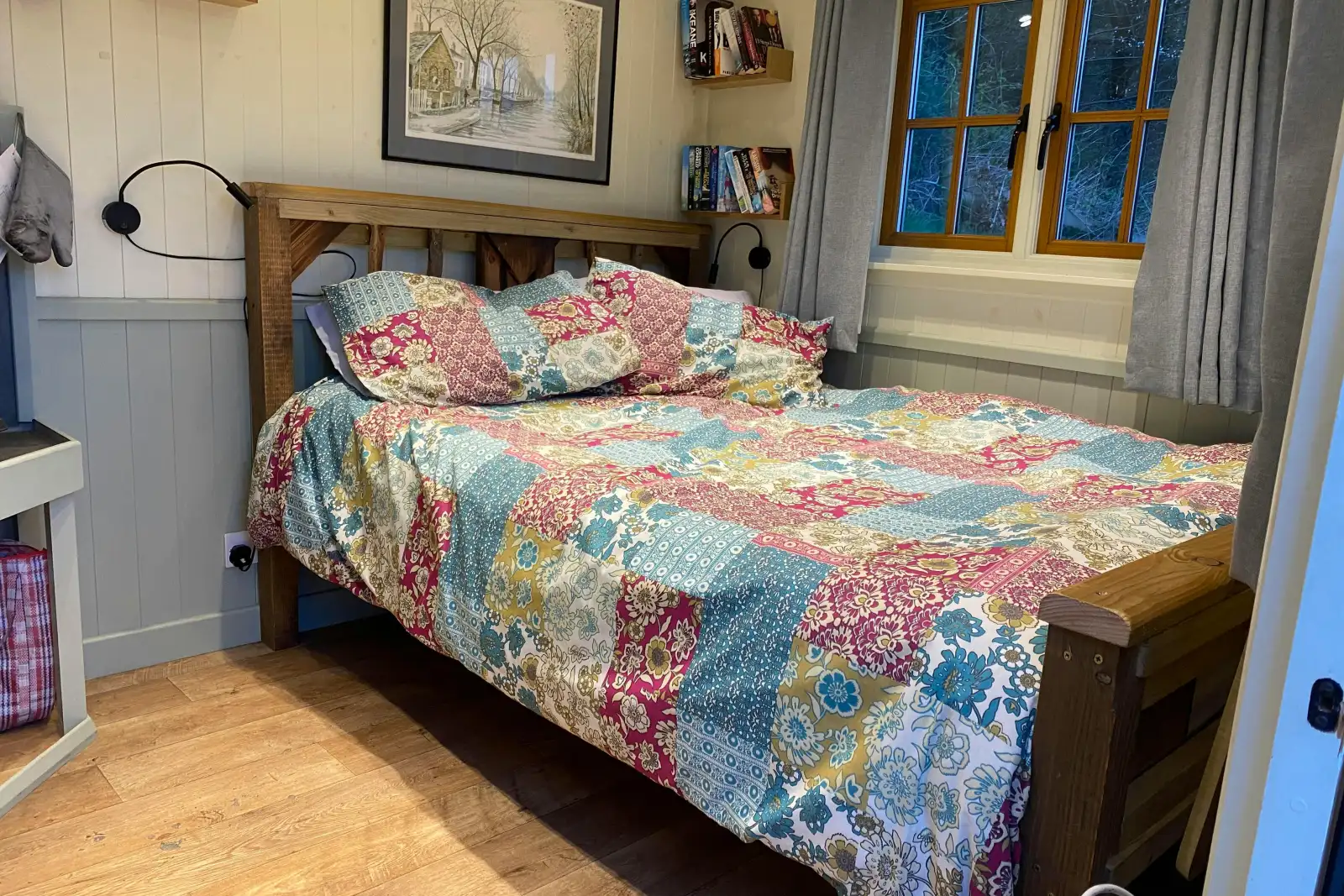 Double bed with patterned quilt cover and pillows with shelves of books to the side, wall art