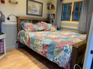 Double bed with patterned quilt cover and pillows with shelves of books to the side, wall art