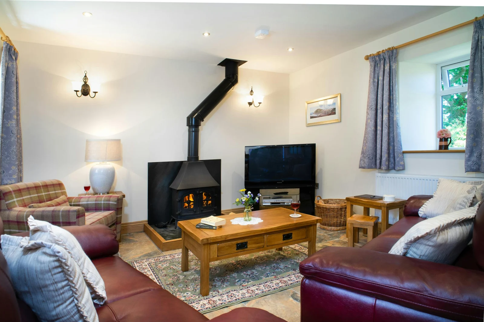 Living room in Towy Cottage, armchair, leather sofas, coffee tables around the log burner and TV