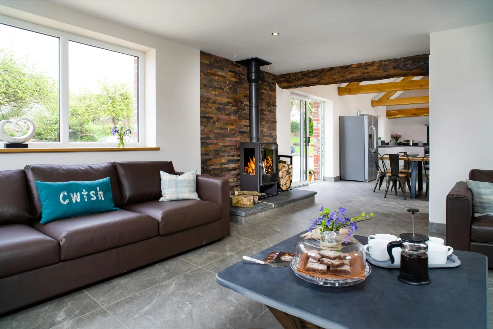 Living room with sofa, log burner, coffee table and view into kitchen