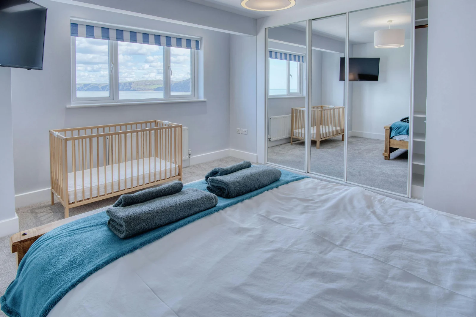 King size bedroom, towels on the bed, cot, window and fitted wardrobe
