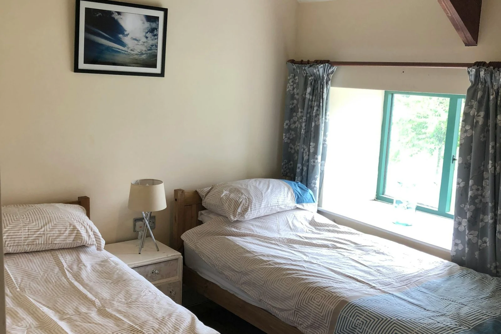 Bedroom with twin single beds, bedside drawers and lamp, low window
