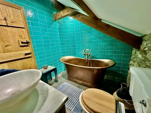 copper bath, toilet with wooden lid, hand wash basin on a marble worktop. Blue wall tiles.