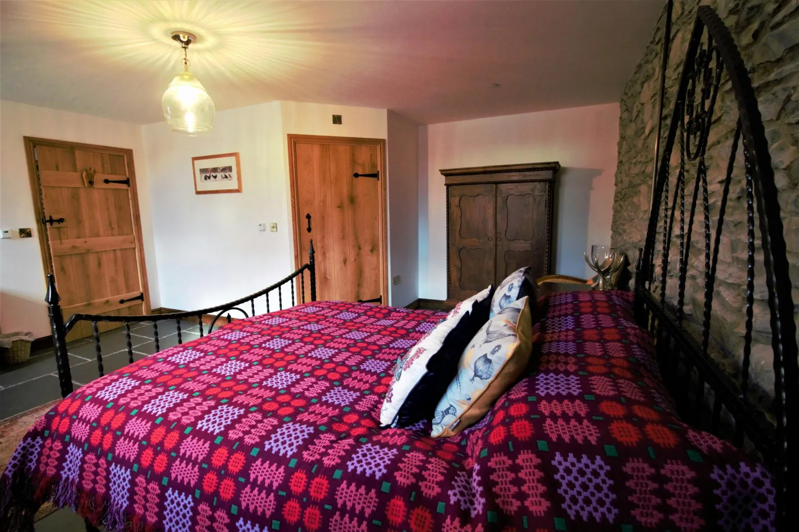 King size bed covered in a Welsh blanket, wardrobe and cushions on the bed