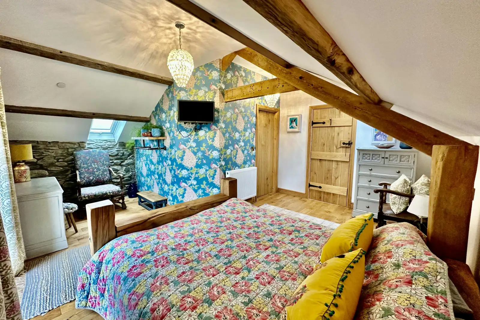 King size bed, floral throw, cushions, patterned wallpaper, wall mounted tv, chest of drawers