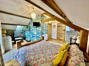 King size bed, floral throw, cushions, patterned wallpaper, wall mounted tv, chest of drawers