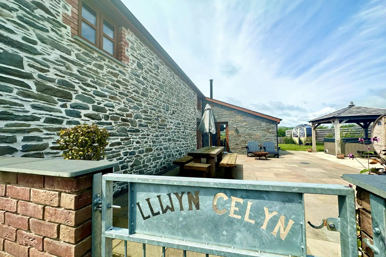 gate to cottage with name on and patio area with picnic bench, pergola and hot tub area