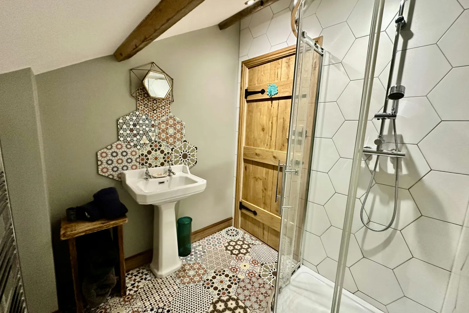 Walk in shower, patterned floor and a few wall tiles, hand wash basin and wooden washing basket