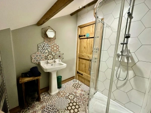 Walk in shower, patterned floor and a few wall tiles, hand wash basin and wooden washing basket