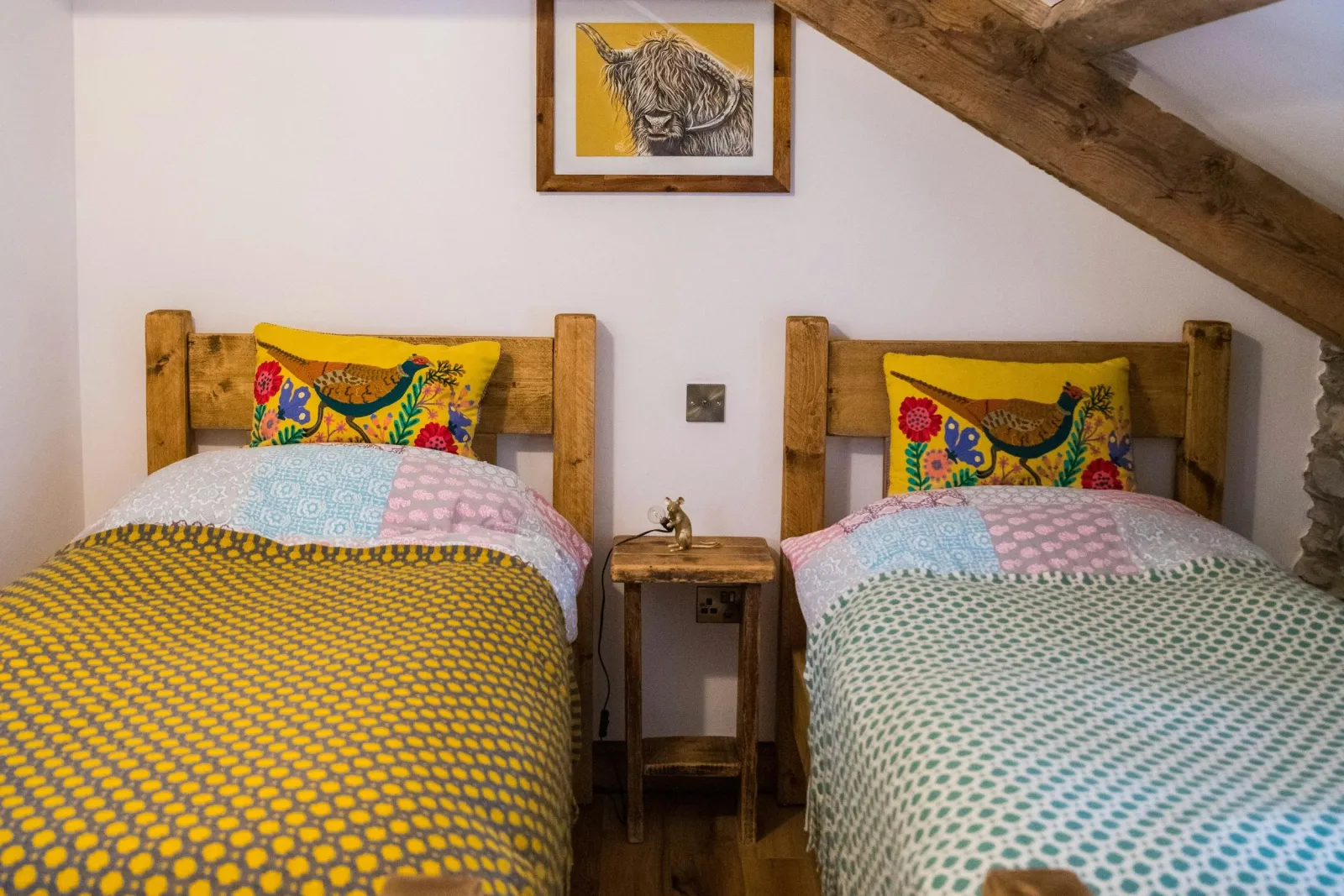 twin beds, bedside table and wall art between beds, exposed wooden beams on ceiling.