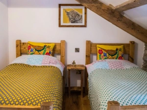 twin beds, bedside table and wall art between beds, exposed wooden beams on ceiling.