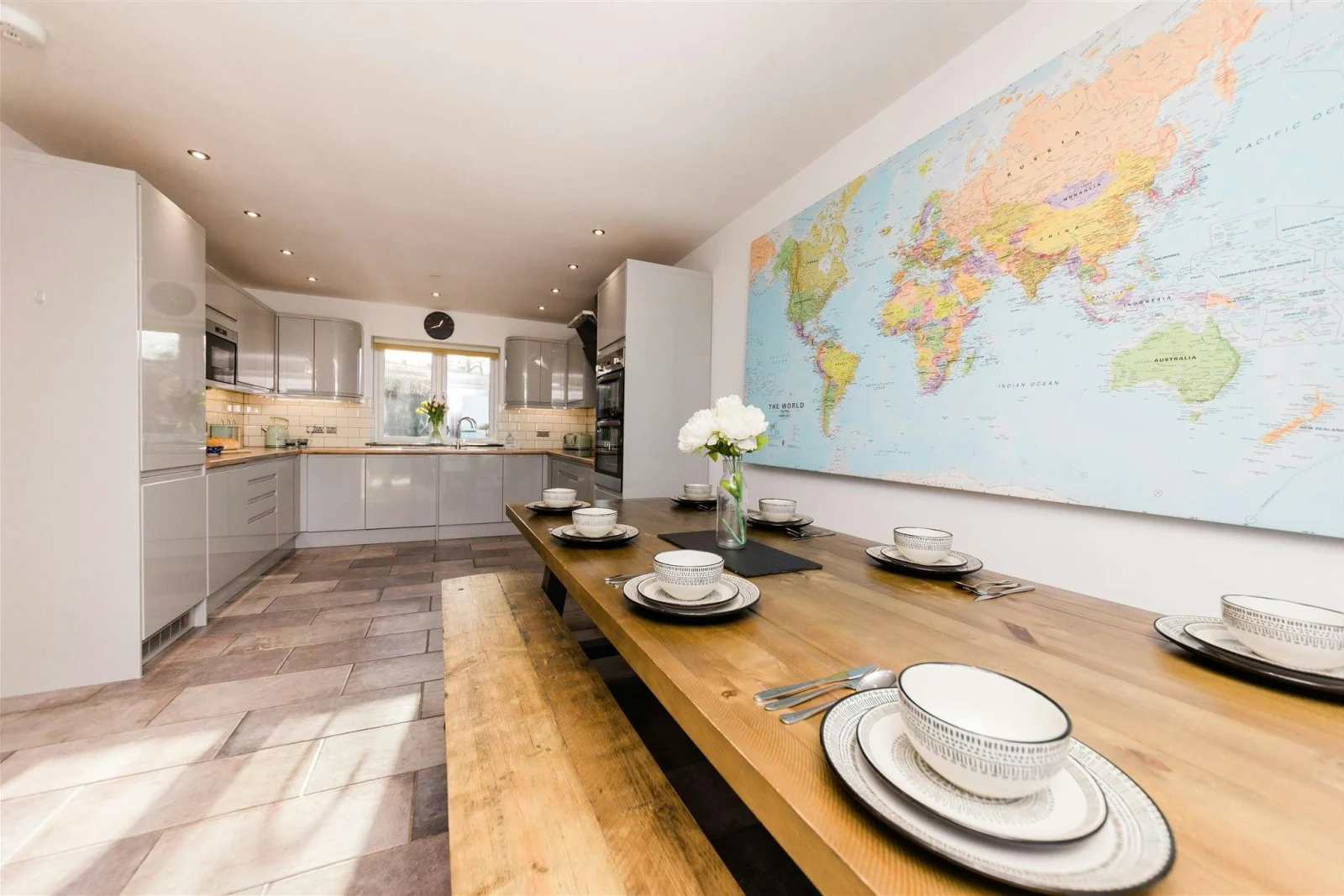 Map of the world on the wall, table and benches laid for lunch with kitchen in background