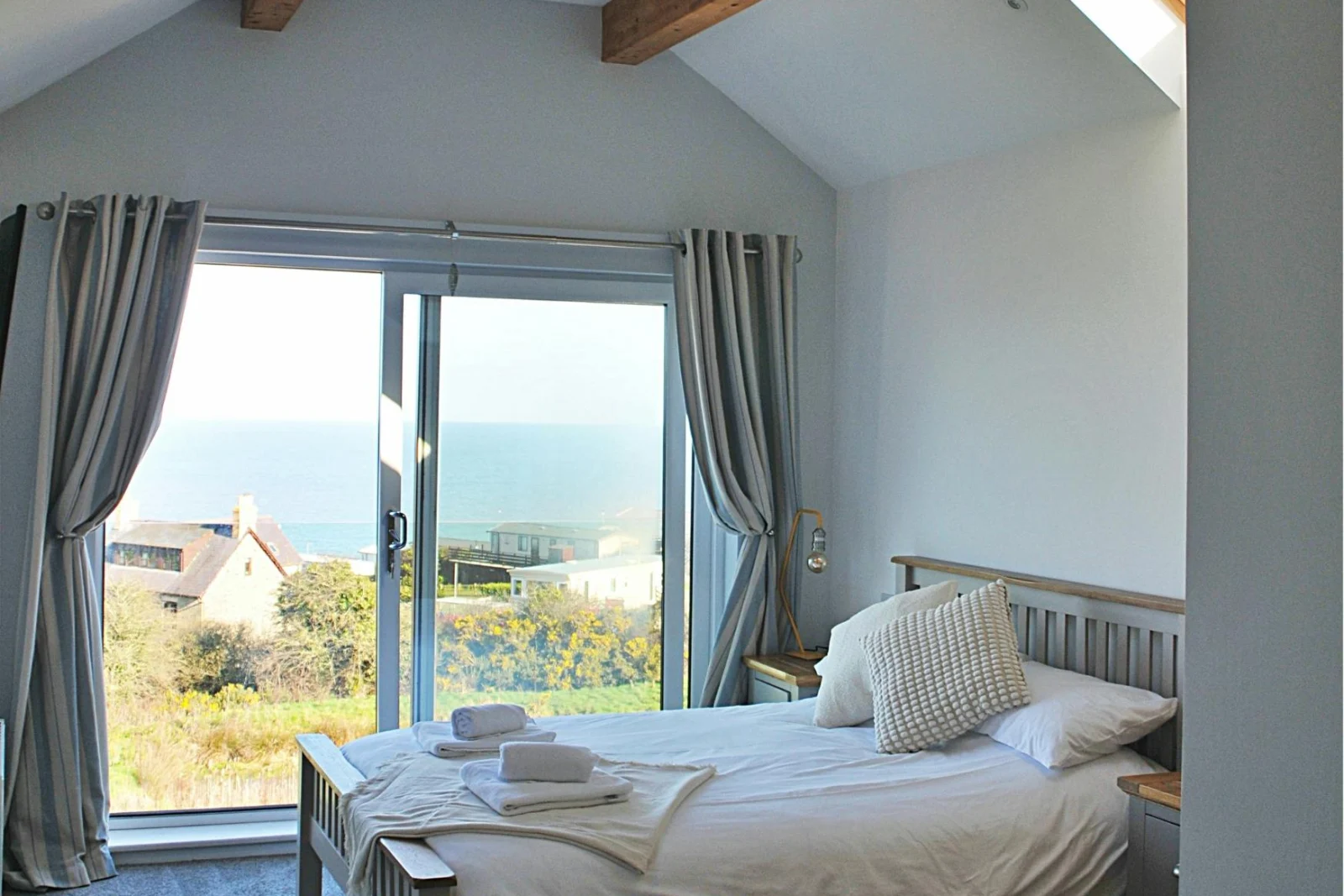 kingsize bed with bedside table and lamp. Patio doors with views to sea