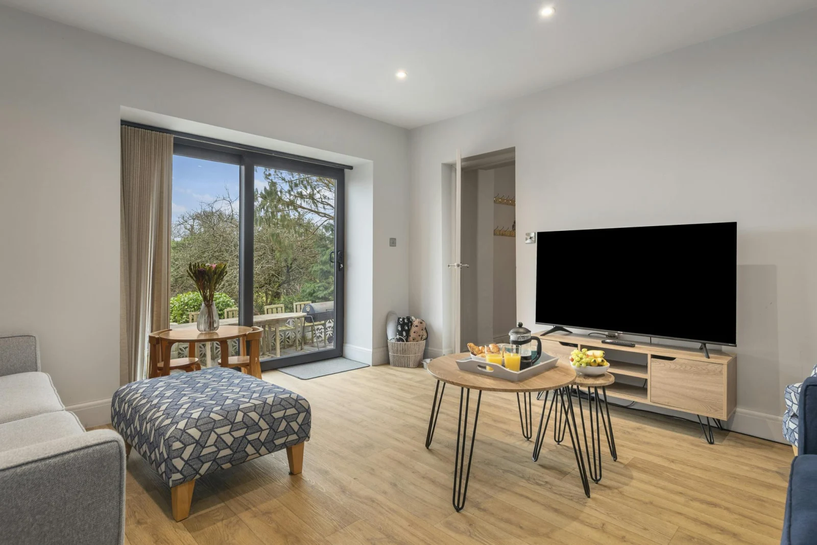 Living room with sofa, patterned ottoman, coffee table and TV on a wooden stand