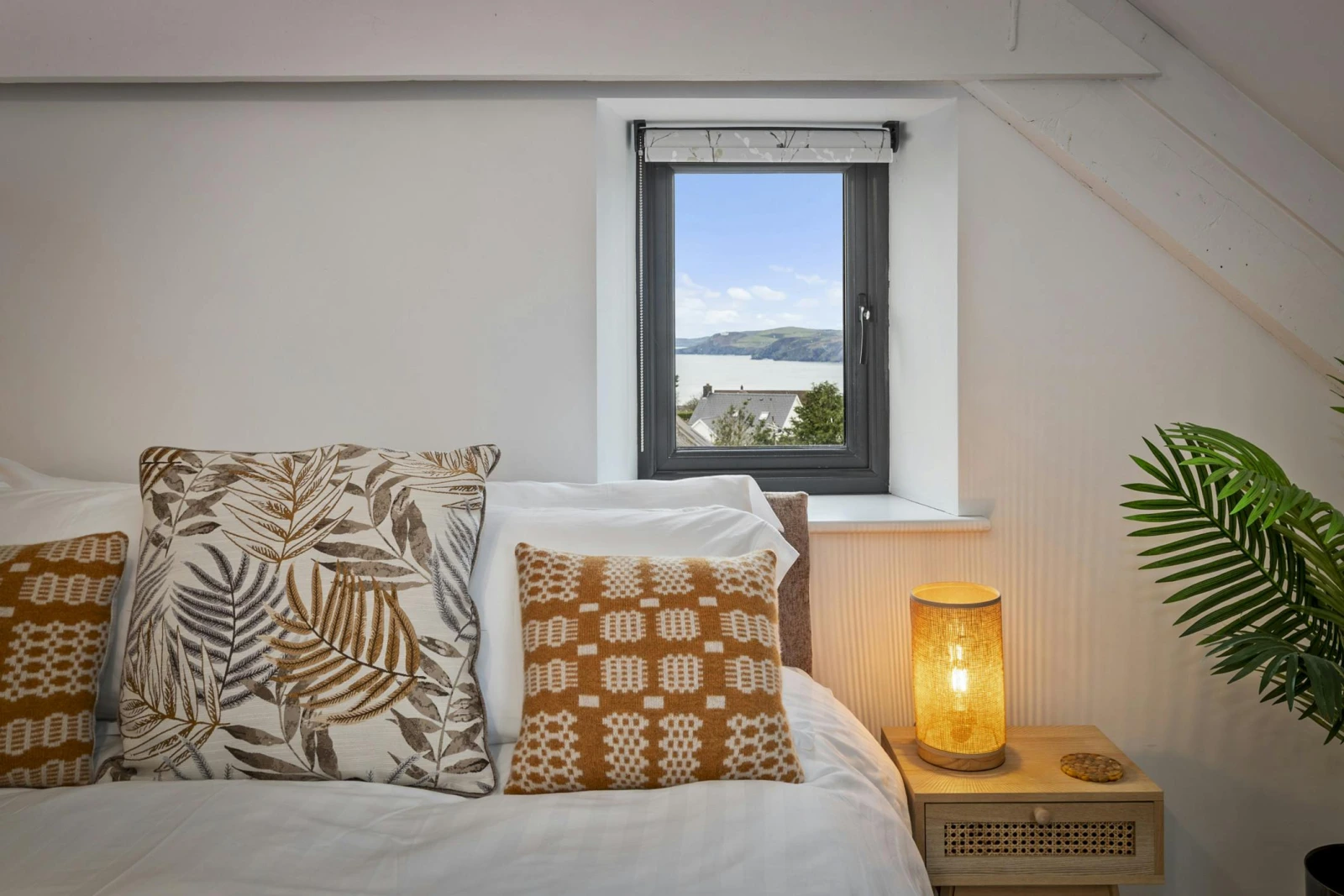 Bedroom corner with bed, two cushions, bedside lamp and small window view