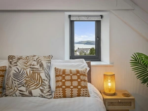 Bedroom corner with bed, two cushions, bedside lamp and small window view