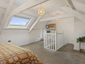 Loft bedroom with white beams, skylight, carpeted floor and stair railing