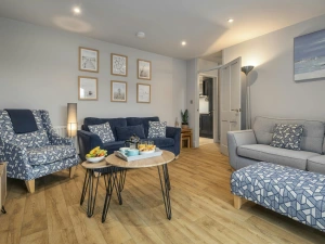 Living room with grey sofa, patterned armchair and footstool, and round coffee table with snacks