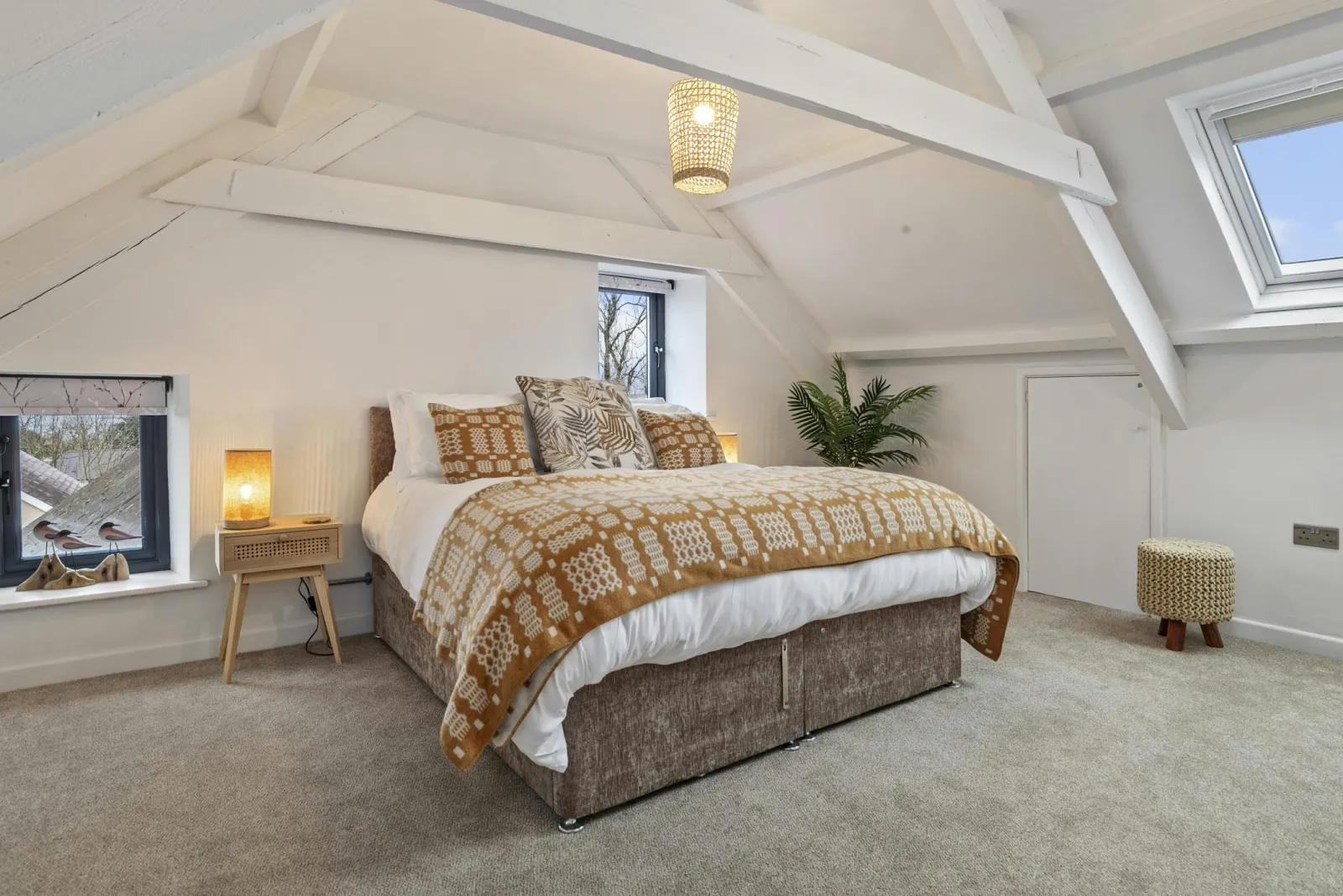 Bedroom with double bed, patterned duvet, bedside table and lamp under sloped ceiling