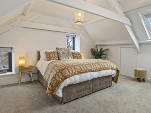 Bedroom with double bed, patterned duvet, bedside table and lamp under sloped ceiling