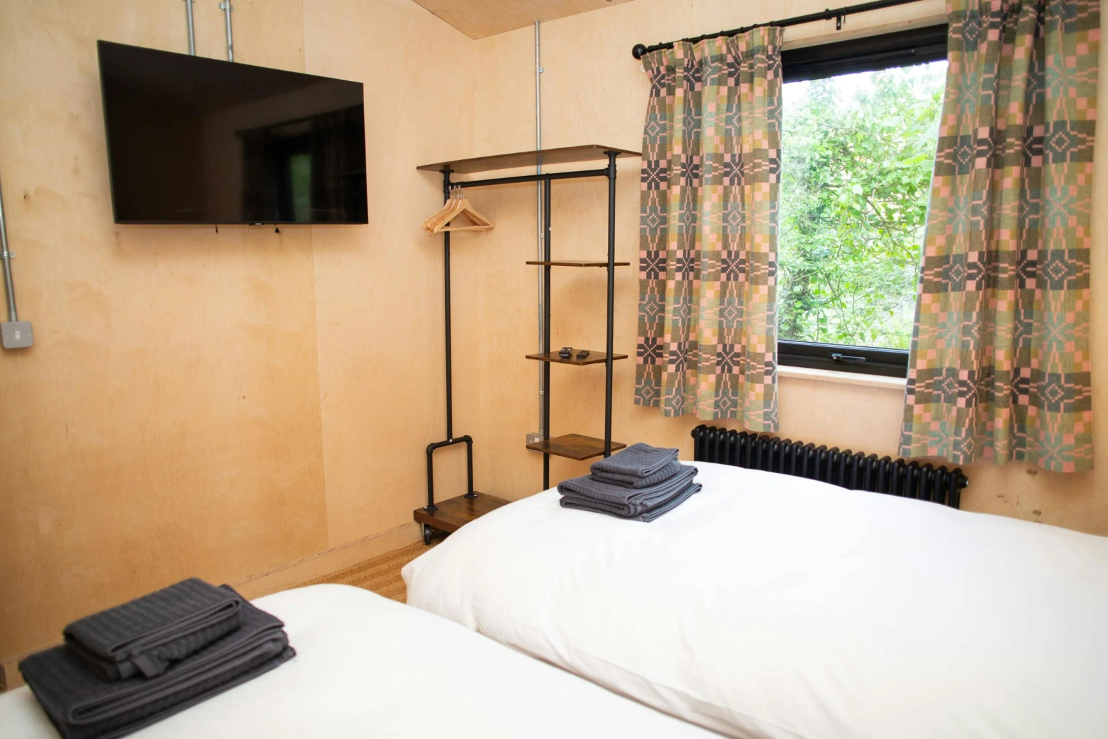 Twin bedroom with clothes hanging rail and wall mounted TV
