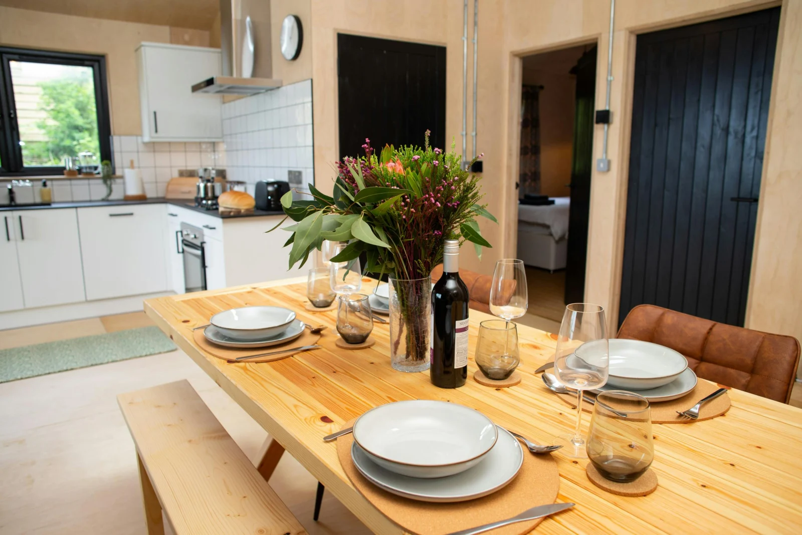 Dining area with table bench and two chairs. Laid for dinner with a vase of flowers